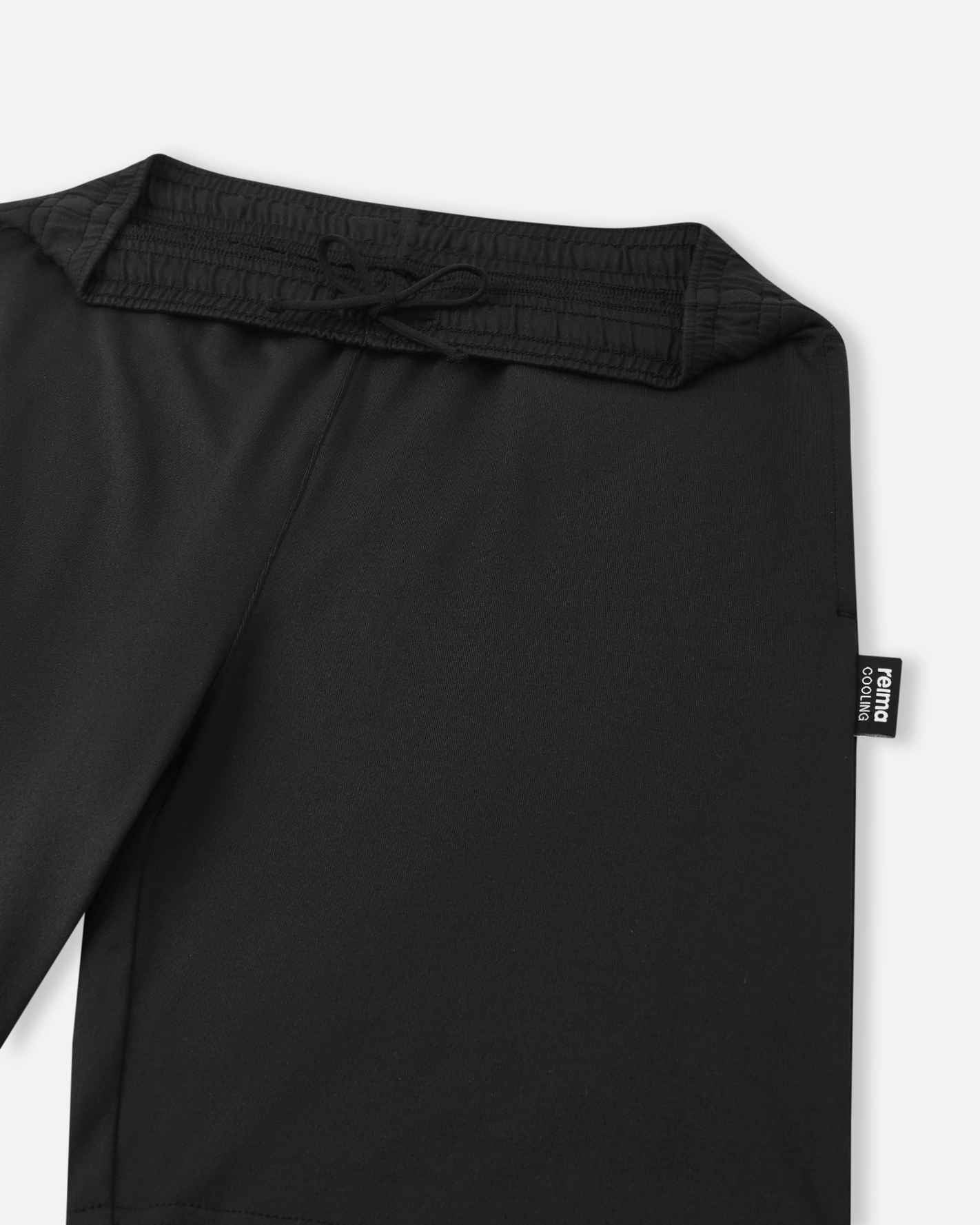 A close-up view of the gathered elastic waistband and black adjustable drawstring on the black Reima Ilmassa shorts. A small black Reima logo tag is visible on the side seam.