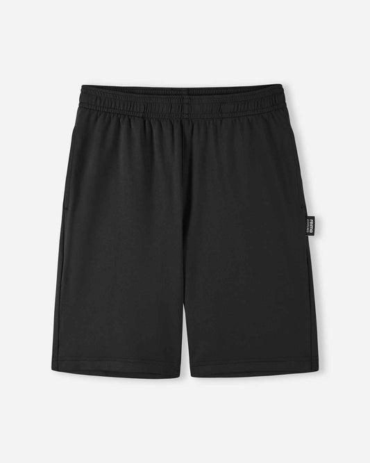 Front view of the Reima Ilmassa kids sunproof shorts in solid black, featuring an elastic waistband, side pockets, and a small logo tag on the left side seam.