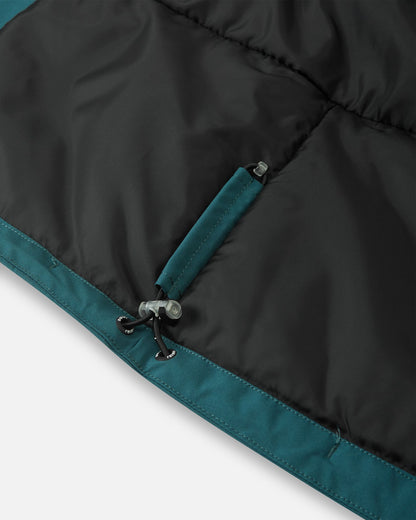 Detail of the interior adjustable hem on the dark teal Reima Jatuni kids' ski jacket, showing the elastic bungee cord and toggle system for a secure, draft-blocking custom fit.