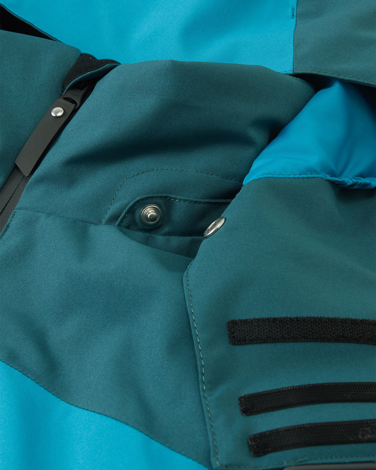Close-up detail of the smooth protective collar and the safe, easy-to-use snap button attachments for the hood on the dark teal Reima Jatuni kids' ski jacket.