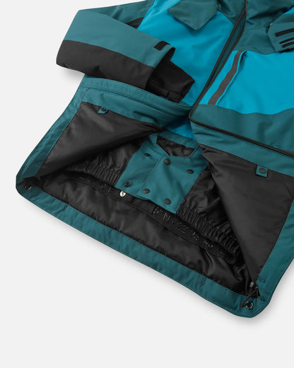 Interior view of the dark teal Reima Jatuni kids' ski jacket, revealing the built-in adjustable snow skirt with snap buttons designed to keep snow out during alpine skiing and snowboarding.