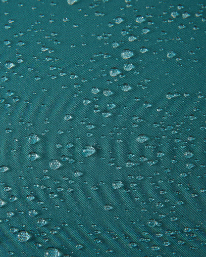 Macro close-up of water droplets actively beading and rolling off the dark teal outer shell of the Reima Jatuni kids' ski jacket, demonstrating the highly effective waterproof and breathable Reimatec membrane.