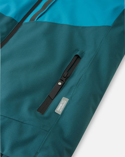 Close-up of a zippered hand pocket on the dark teal Reima Jatuni kids' ski jacket, featuring a Reimatec waterproof tag indicating premium weather protection and extreme durability.