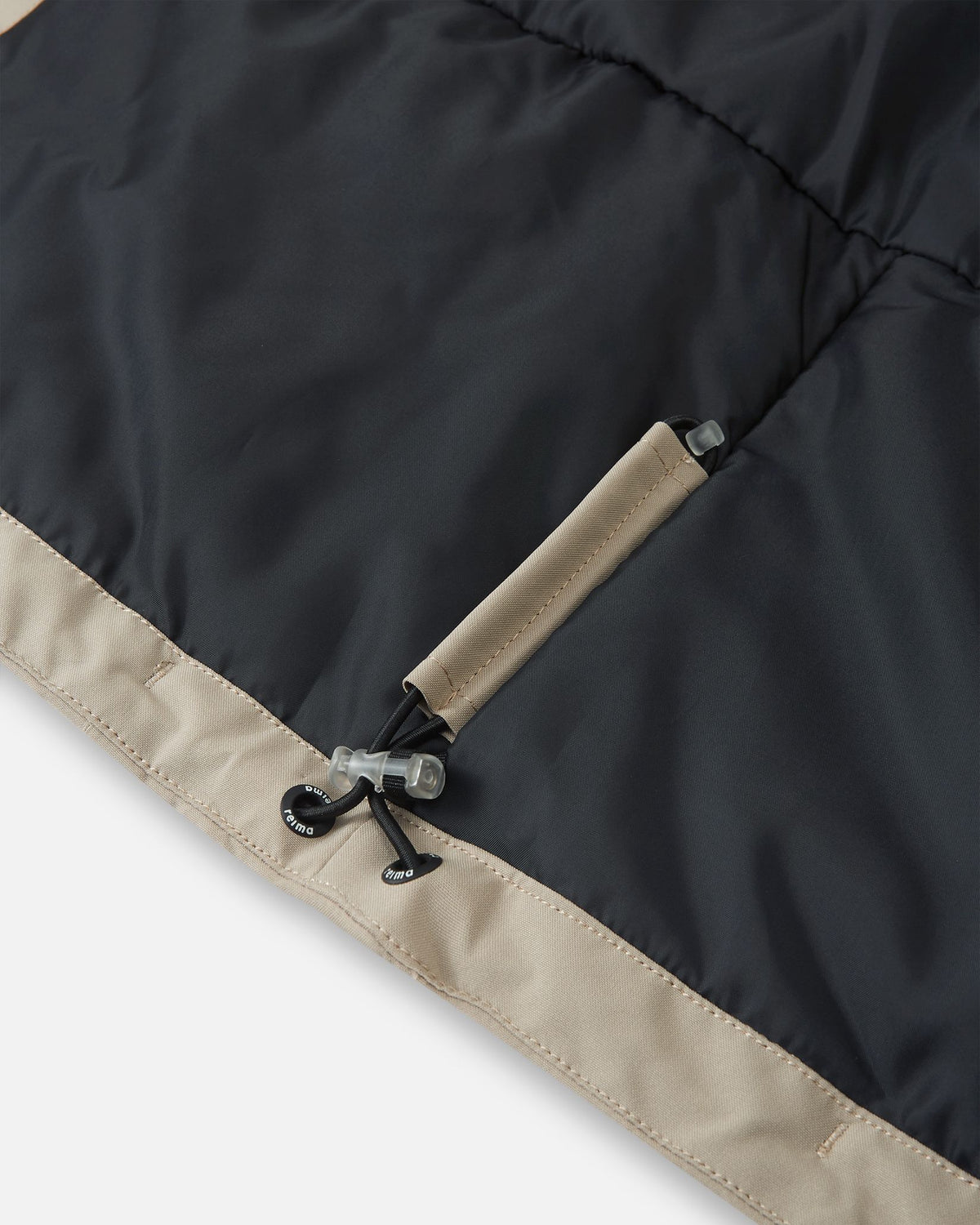 Detail of the interior adjustable hem on the earthy beige Reima Jatuni kids' ski jacket, showing the elastic bungee cord and toggle system for a secure, draft-blocking custom fit.