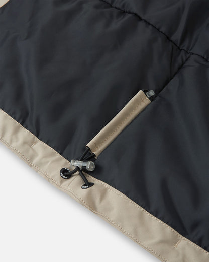 Detail of the interior adjustable hem on the earthy beige Reima Jatuni kids' ski jacket, showing the elastic bungee cord and toggle system for a secure, draft-blocking custom fit.