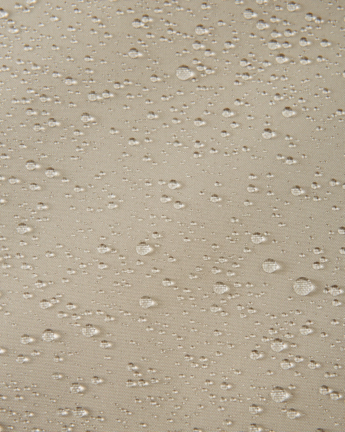 Macro close-up of water droplets actively beading and rolling off the earthy beige outer shell of the Reima Jatuni kids' ski jacket, demonstrating the highly effective waterproof and breathable Reimatec membrane.
