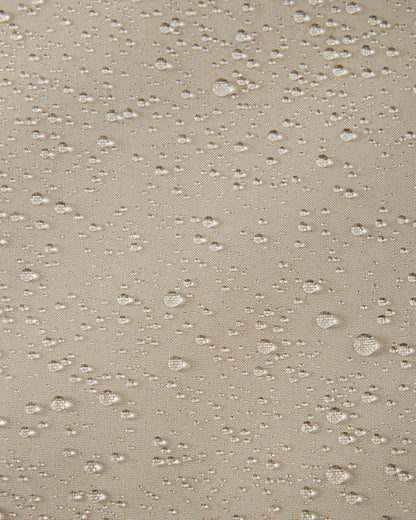 Macro close-up of water droplets actively beading and rolling off the earthy beige outer shell of the Reima Jatuni kids' ski jacket, demonstrating the highly effective waterproof and breathable Reimatec membrane.