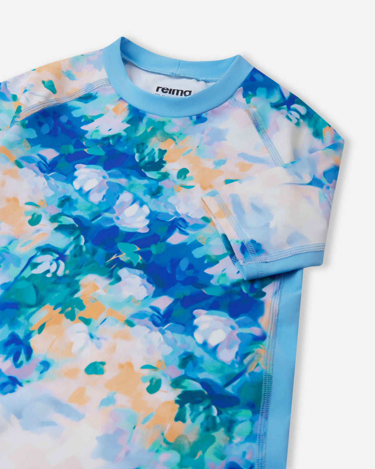 Close-up detail of the Reima Joonia girls' sunproof rash guard in fresh blue, highlighting the protective stretch-knit crew collar, durable flatlock seams, and stylish pastel floral pattern.