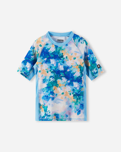 Front view of the Reima Joonia girls' UPF 50+ sunproof rash guard, featuring a vibrant fresh blue and pastel watercolor floral print, designed with comfortable short raglan sleeves for active beach days.