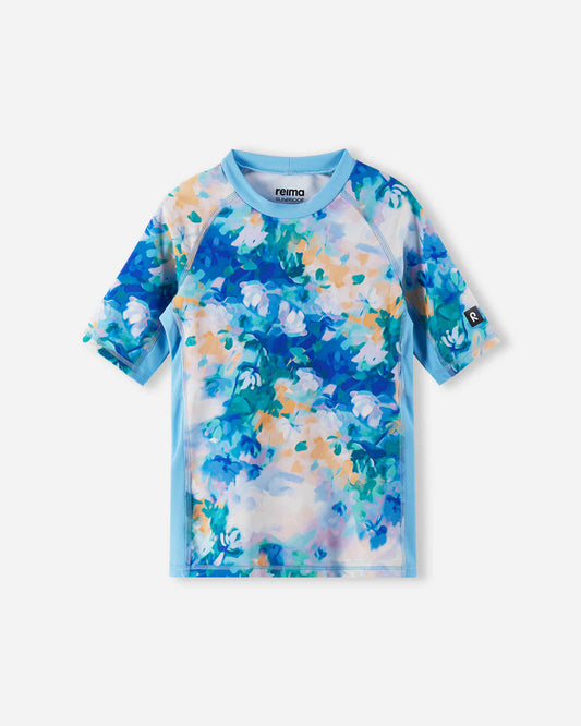 Front view of the Reima Joonia girls' UPF 50+ sunproof rash guard, featuring a vibrant fresh blue and pastel watercolor floral print, designed with comfortable short raglan sleeves for active beach days.