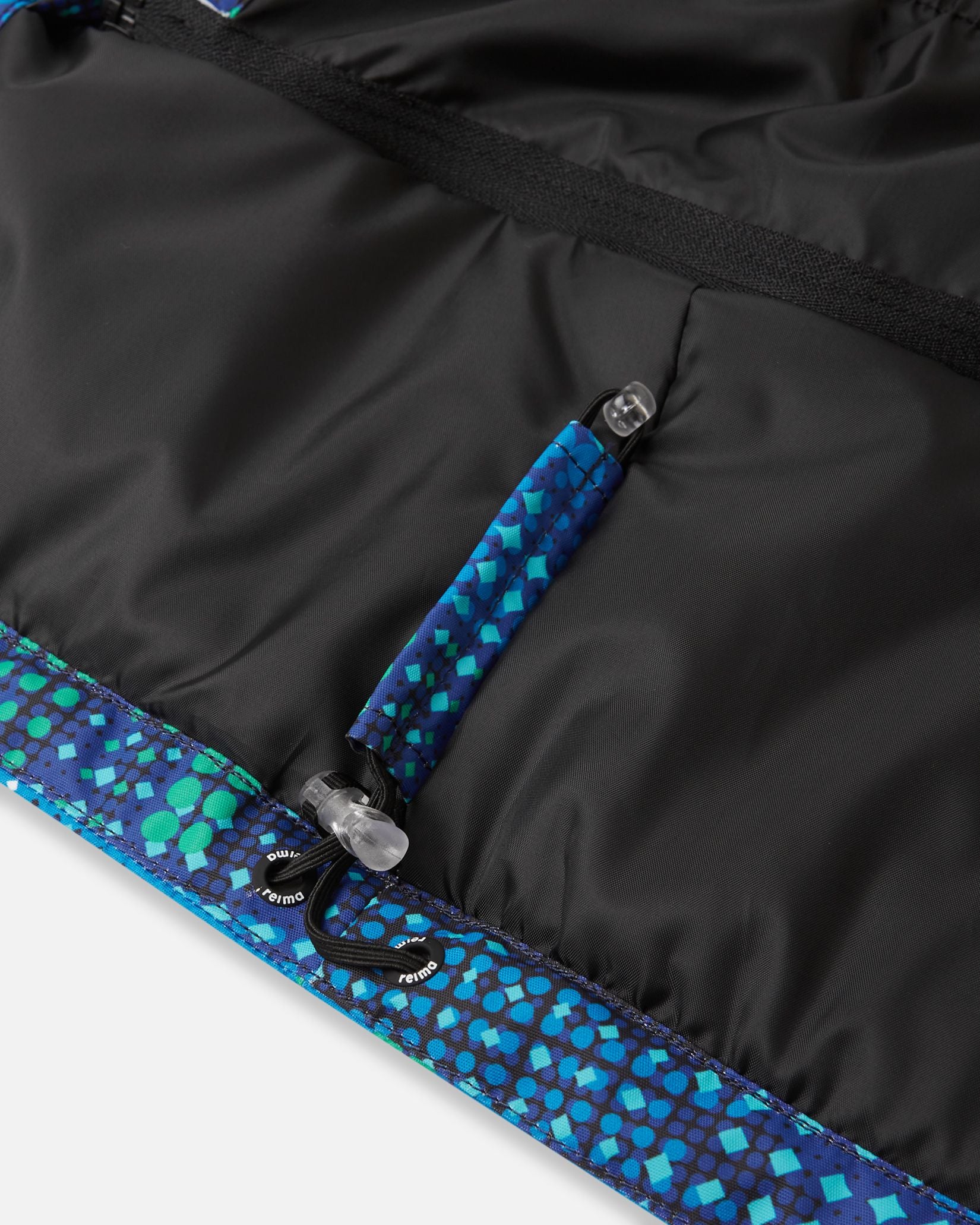 Close-up detail of the adjustable bottom hem on the twilight blue Reima Kairala boys' winter snow coat, featuring a secure bungee drawcord and toggle system designed to cinch tight and seal out cold drafts and snow.