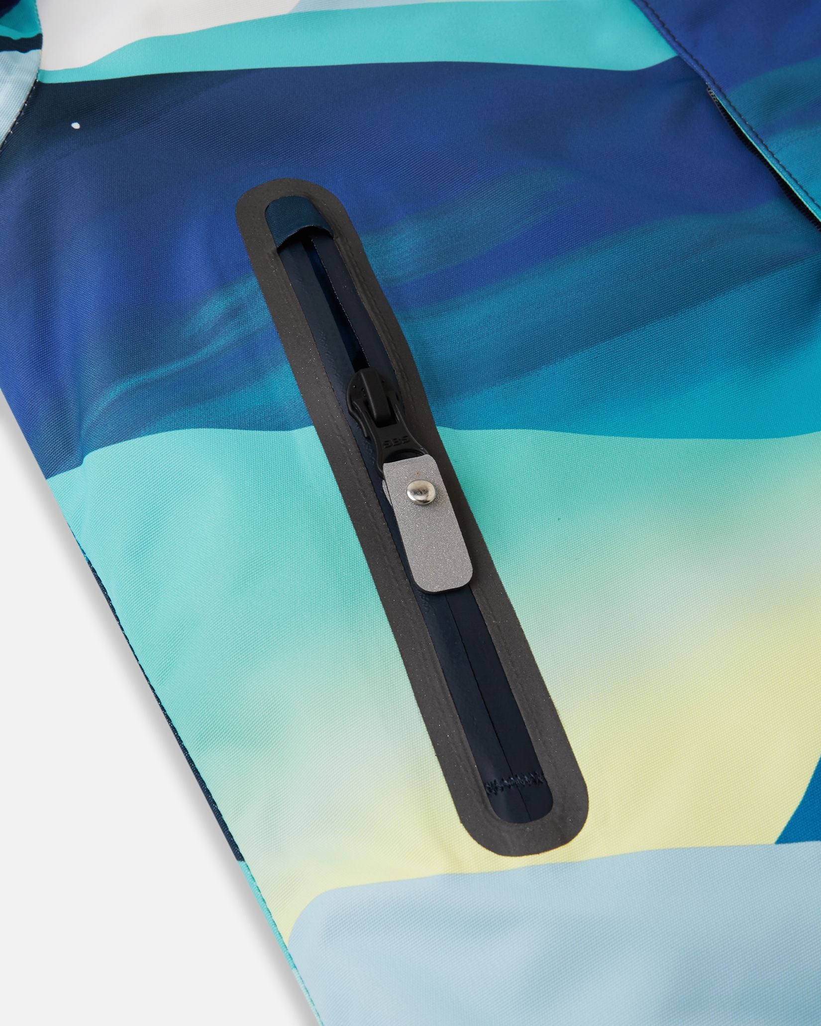 Close-up of the sealed, water-resistant zipper pocket on the front panel of the bright blue Reima Kairala kids' winter ski jacket, showcasing the durable construction.