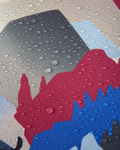Macro detail of the soft black, blue, and red mountain print Reimatec fabric used on the Reima Kairala kids' ski jacket, demonstrating its waterproof technology with dense water droplets beading and resting on the breathable surface.