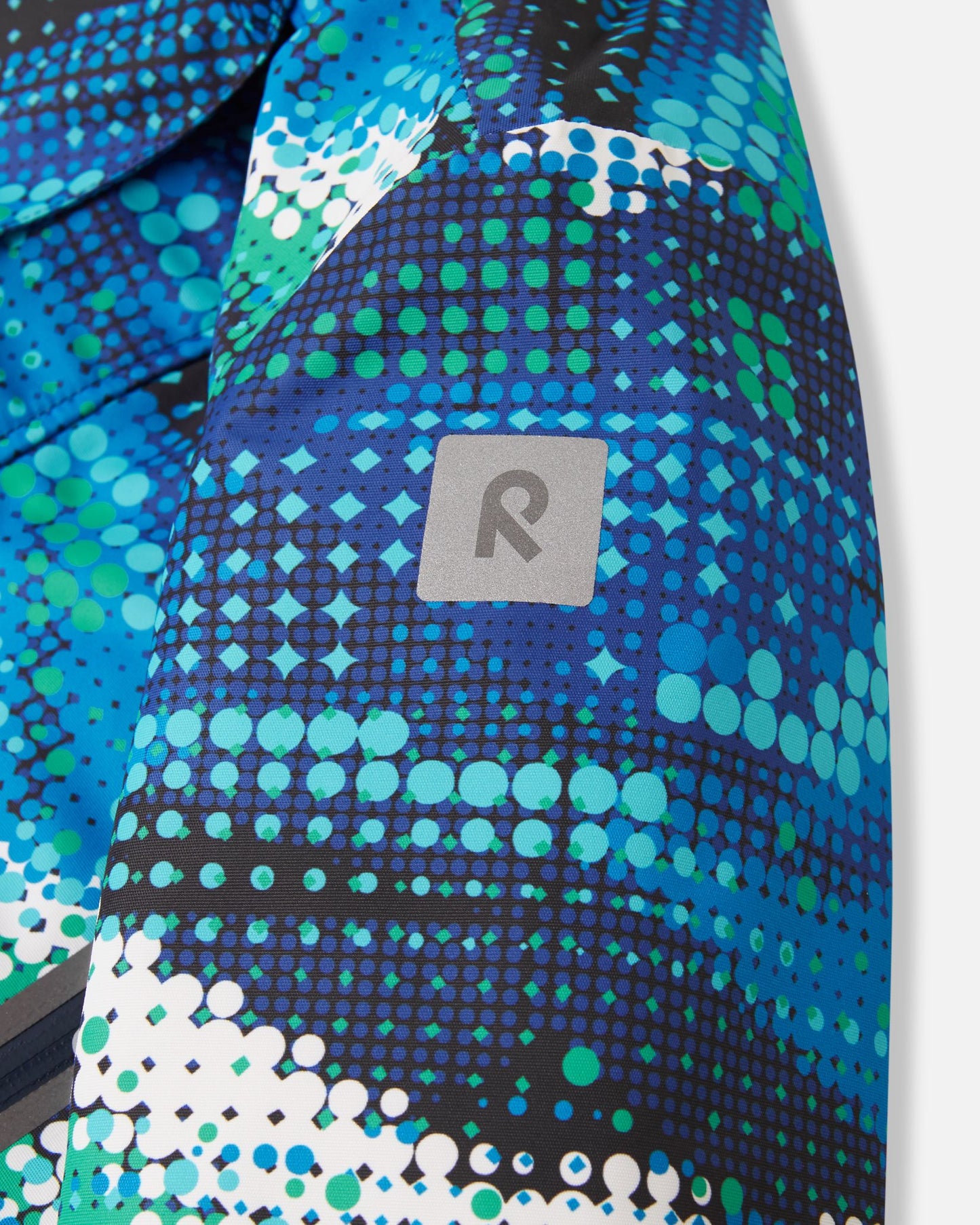Close-up of the safety-enhancing reflective Reima logo patch on the sleeve of the twilight blue Kairala kids' waterproof ski jacket, providing essential visibility in low-light winter conditions.
