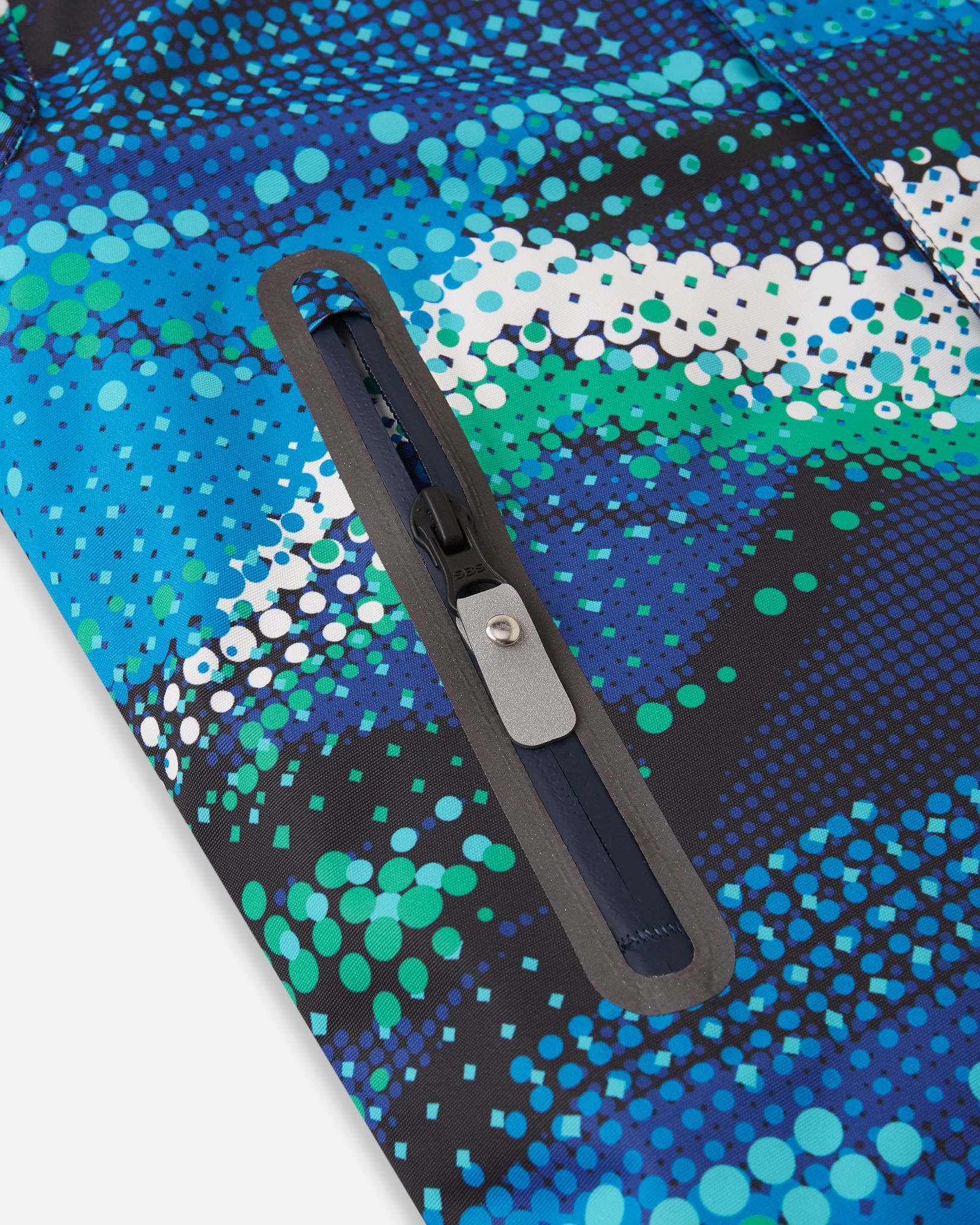 Close-up of the sealed, water-resistant zipper pocket on the front panel of the twilight blue Reima Kairala kids' winter ski jacket, showcasing the durable construction designed for snow sports.