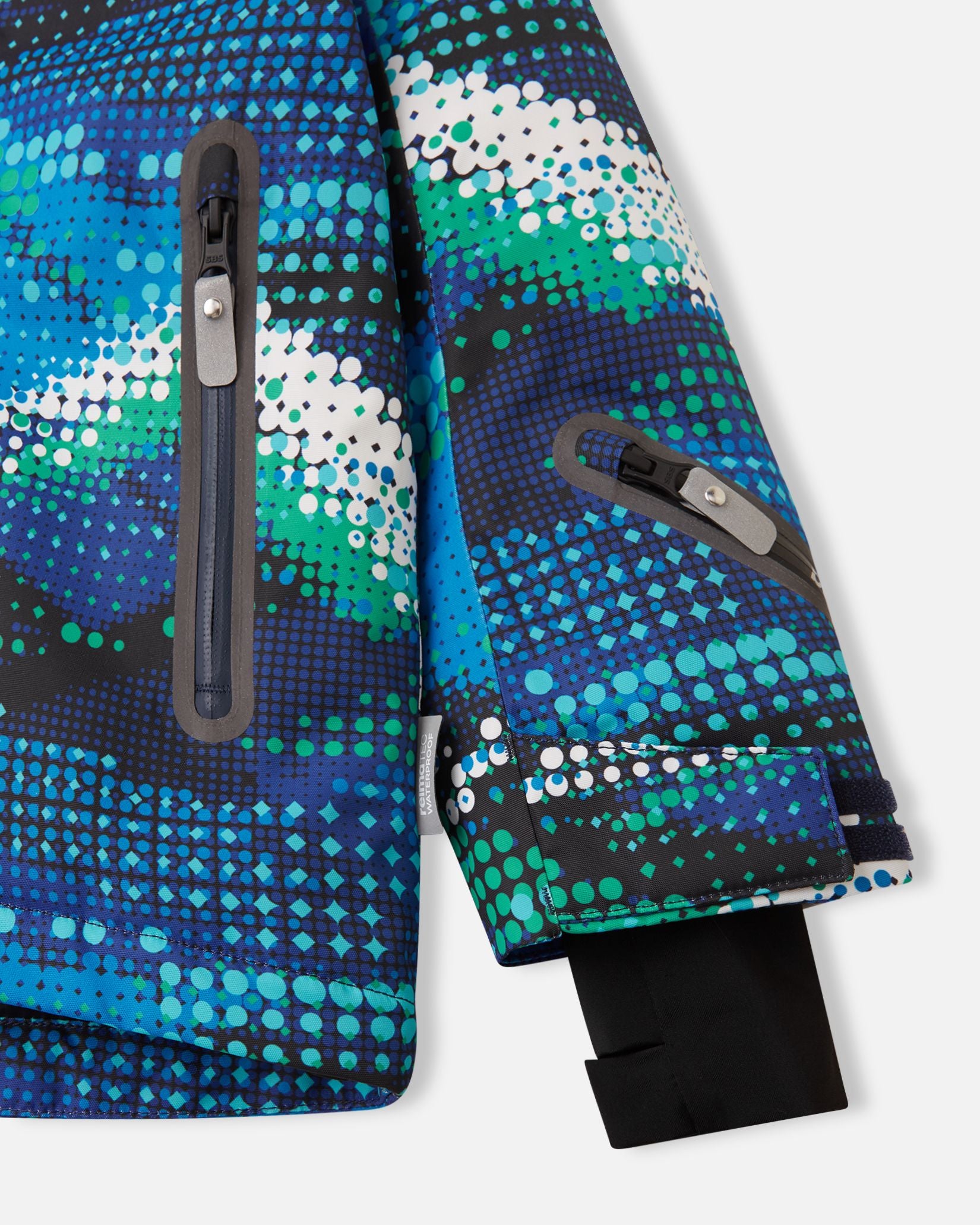 Detail view of the waterproof zippered sleeve ski pass pocket, velcro cuff adjuster, and inner lycra cuff with thumbhole on the twilight blue Reima Kairala kids' ski jacket.