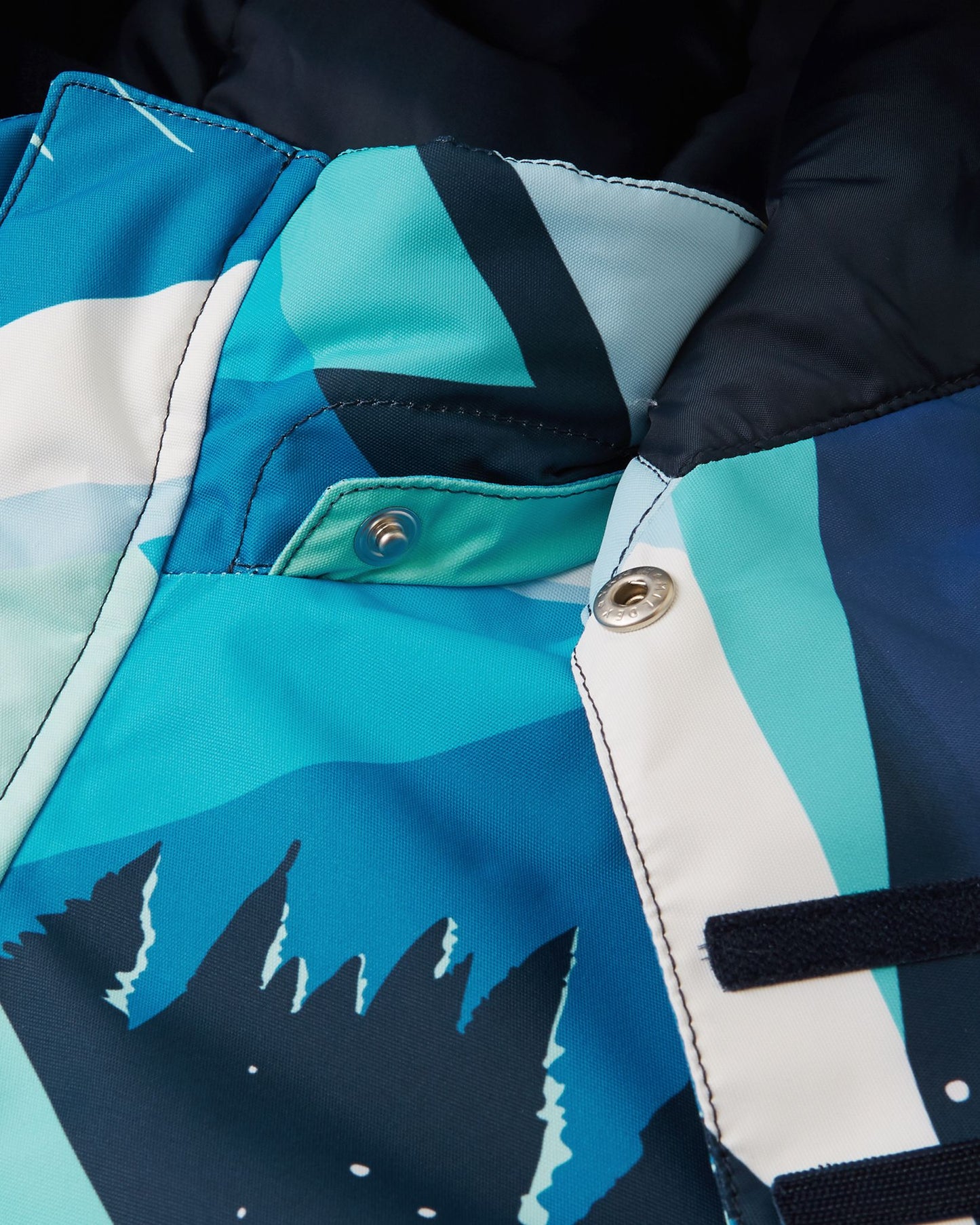 Detailed view of the protective chin guard and sturdy collar snaps on the bright blue Reima Kairala youth snowboard jacket, engineered to block freezing winter winds.