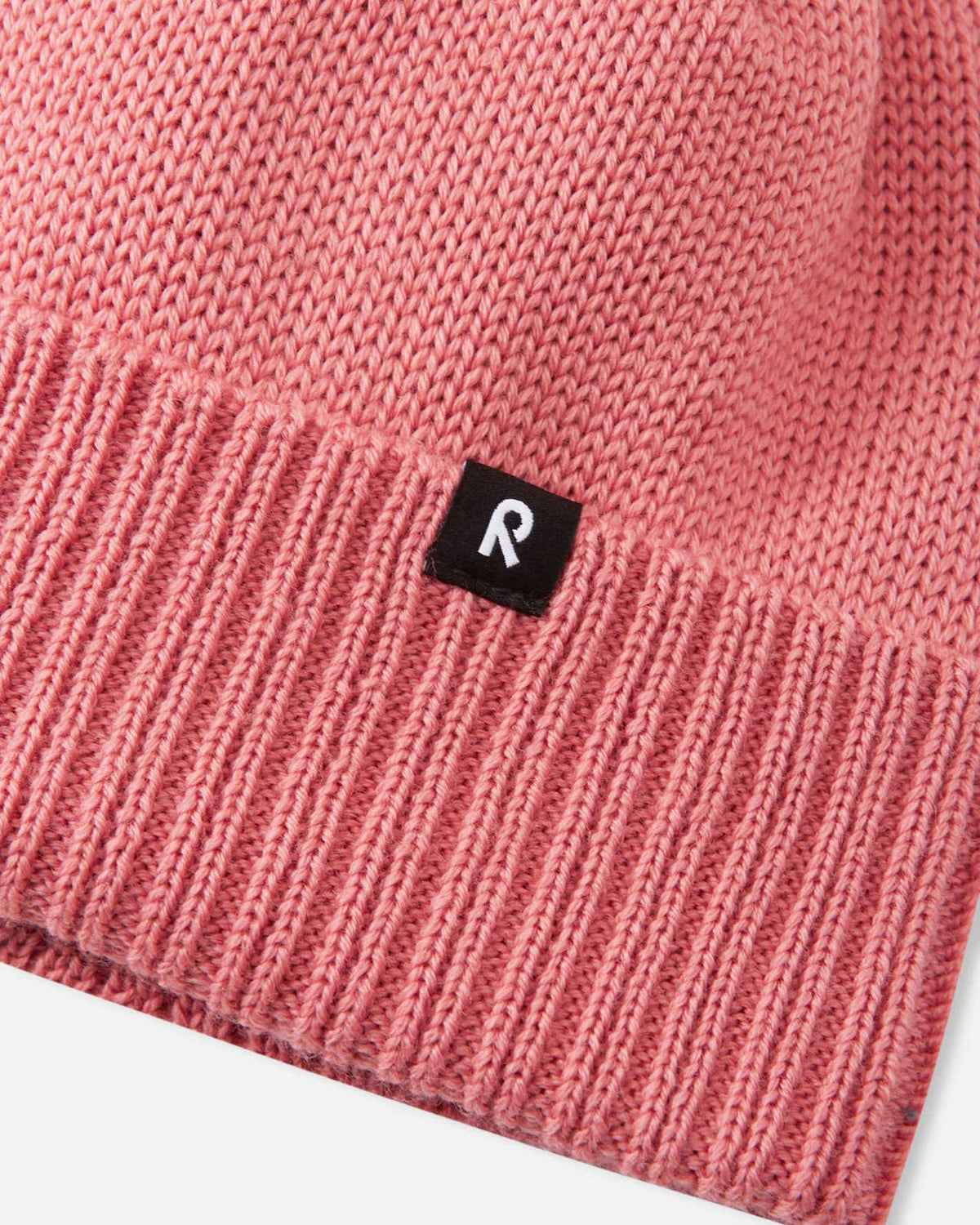 Close-up macro detail of the Reima Kalotti kids' winter beanie in rose blush, highlighting the soft merino wool blend knit, the textured ribbed cuff, and the woven black Reima 'R' brand logo.