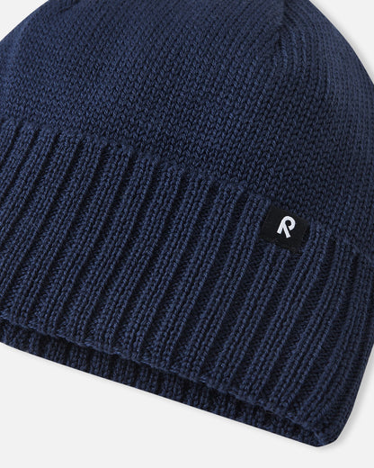 Macro close-up of the premium knitted merino wool texture on the navy blue Reima Kalotti kids' beanie, demonstrating the soft, breathable, and temperature-regulating winter yarn.