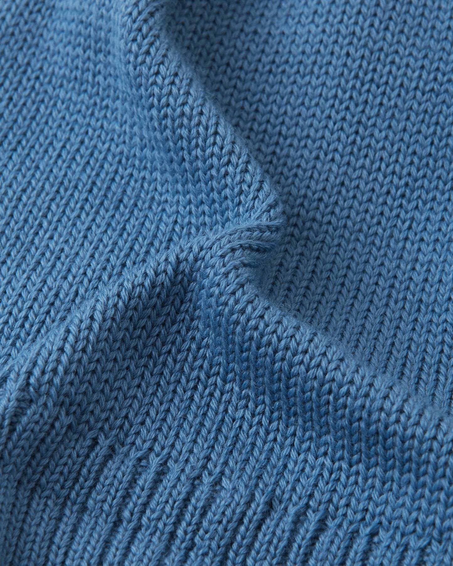 Macro close-up of the premium knitted merino wool texture on the ocean blue Reima Kalotti kids' beanie, demonstrating the soft, breathable, and temperature-regulating winter yarn.