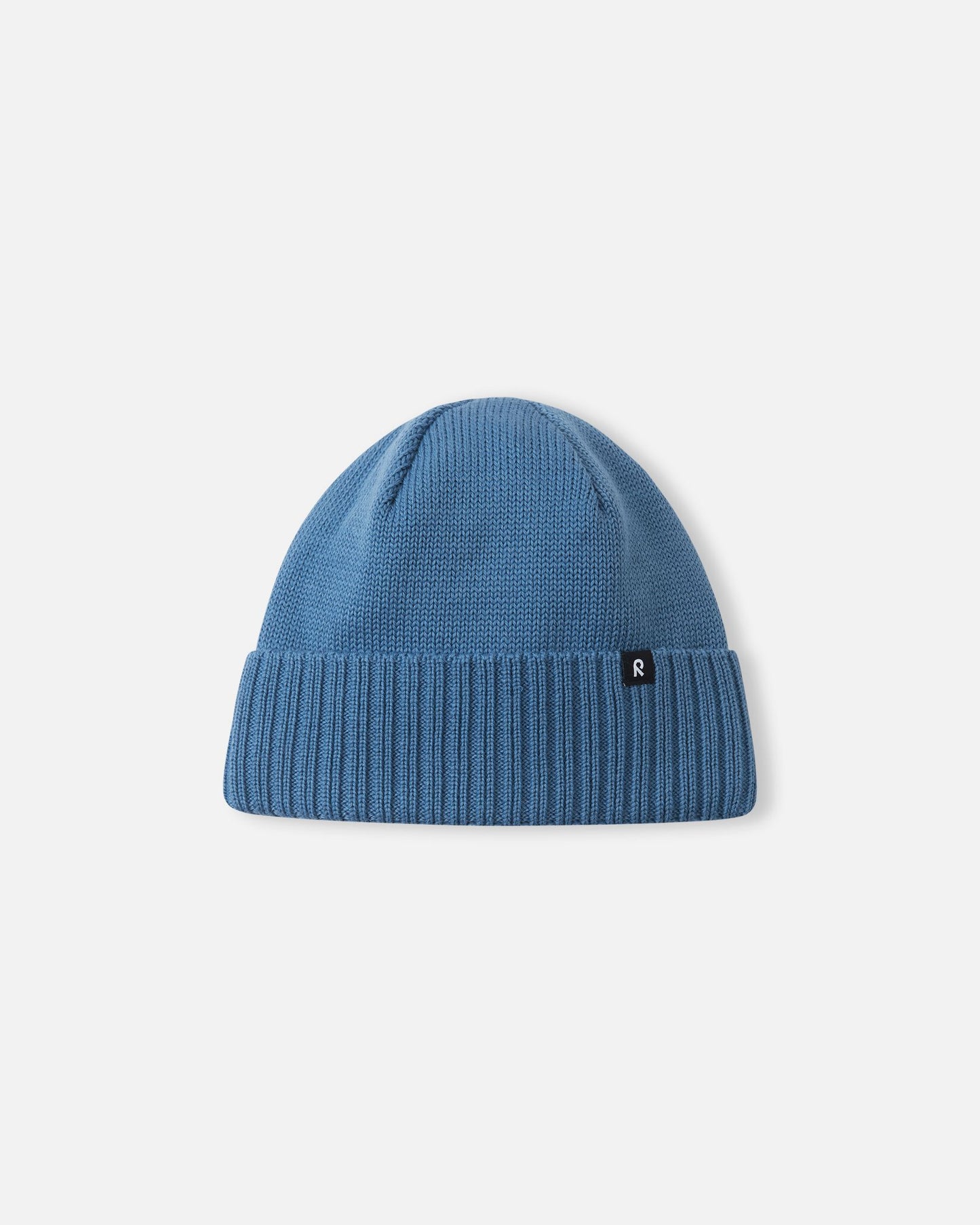 Angled side profile of the ocean blue Reima Kalotti youth merino wool beanie, featuring the small Reima logo tag attached to the ribbed brim.