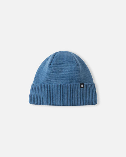Angled side profile of the ocean blue Reima Kalotti youth merino wool beanie, featuring the small Reima logo tag attached to the ribbed brim.