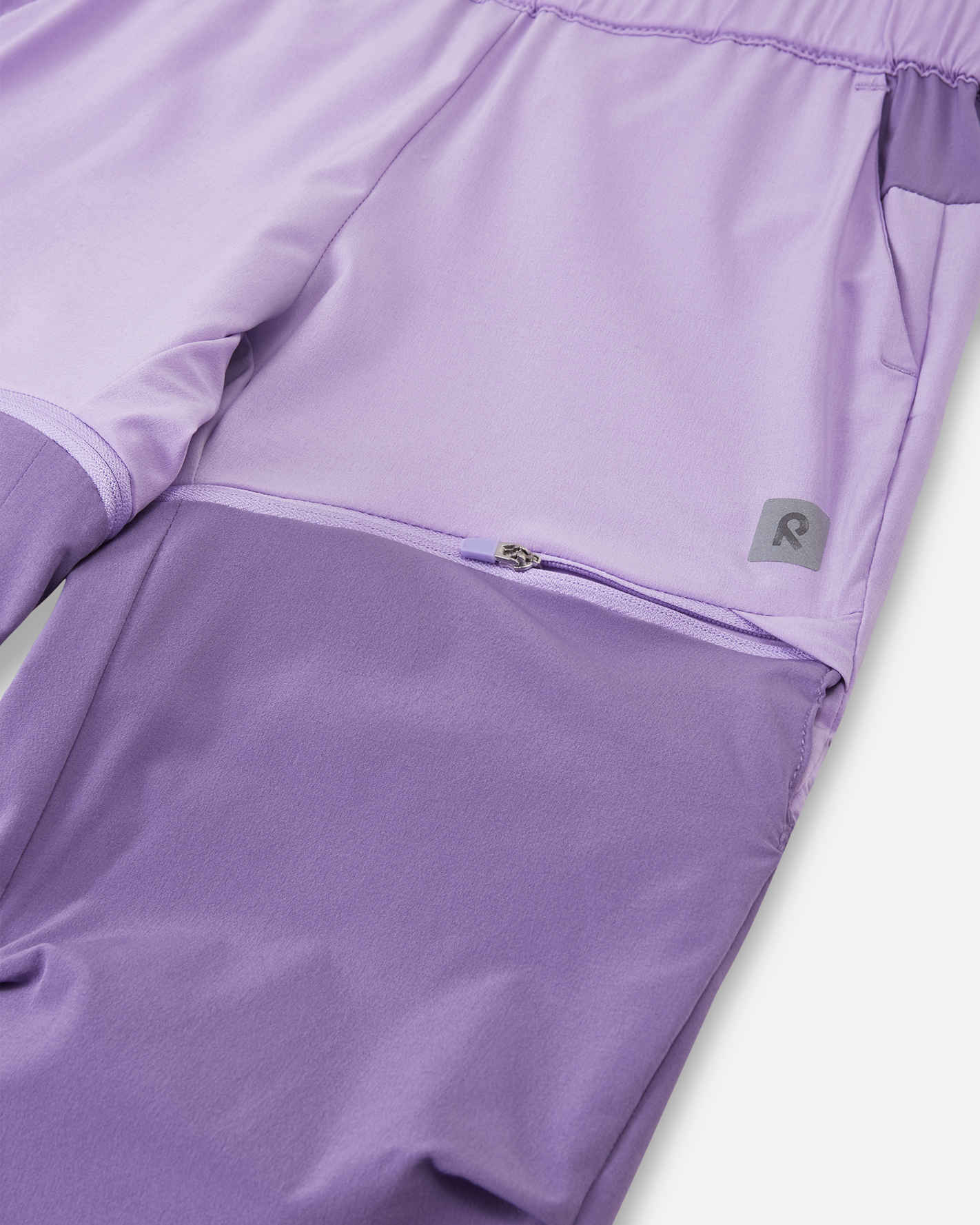 Detailed close-up of the concealed zipper on the Reima Kaveris kids' blooming lilac convertible pants, showing the secure and smooth attachment of the darker purple lower leg panels.