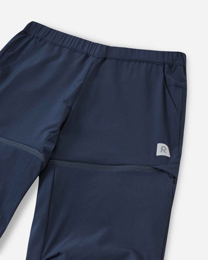 Close-up view of the upper front on the Reima Kaveris kids' navy blue hiking pants, detailing the flexible elastic waistband, deep side pockets, and the small reflective Reima logo patch.