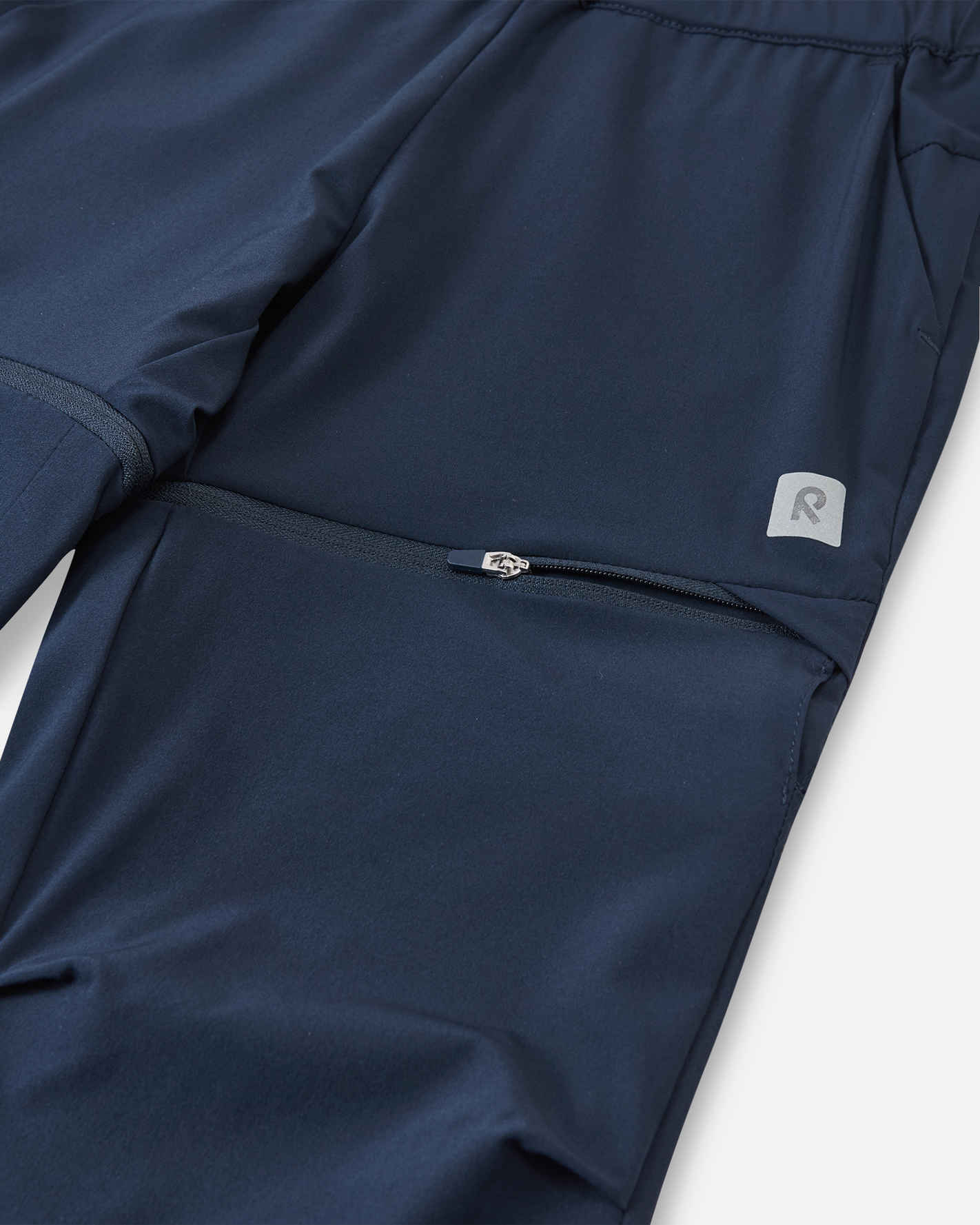 Macro close-up of the hidden zipper detail on the Reima Kaveris kids' navy blue convertible pants, demonstrating the high-quality, easy-to-use hardware designed for quickly detaching the lower pant legs.