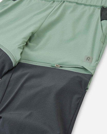 Macro close-up of the hidden zipper detail on the Reima Kaveris kids' stone green convertible pants, showing the durable hardware used to easily detach the dark grey lower leg panels.