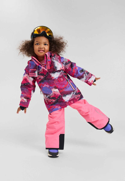 Studio lifestyle portrait of a young girl playfully posing in the rosy berry print Reima Kiiruna ski jacket paired with solid pink snow pants and ski goggles, showcasing the outfit's comfortable, active fit for winter sports.