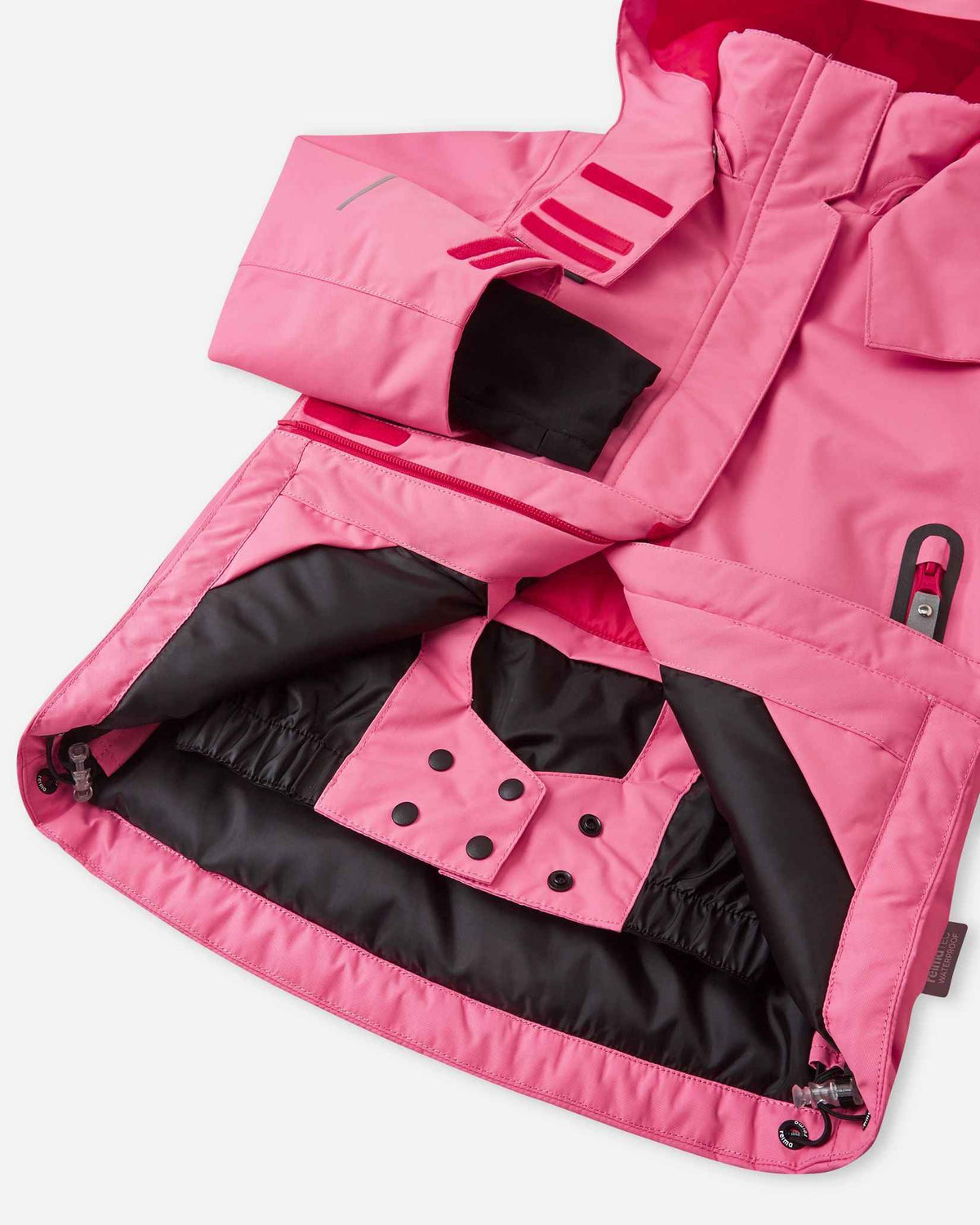 Open interior view of the lower half of the solid soft coral Reima Kiiruna girls' ski jacket, revealing the built-in snap-closure powder skirt and adjustable drawcord hem designed to block deep snow during alpine adventures.