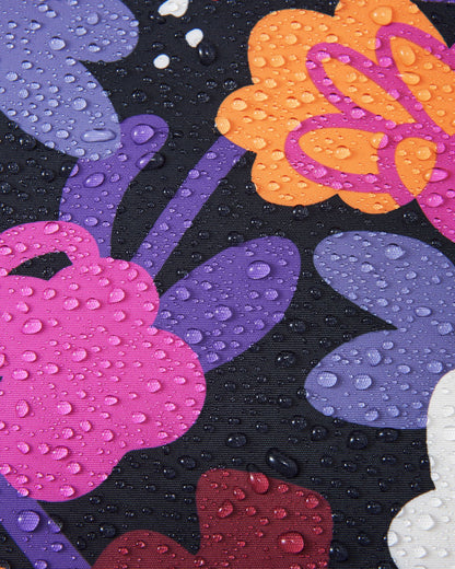 Macro detail of the black floral Reimatec fabric used on the Reima Kiiruna girls' ski jacket, demonstrating its waterproof technology with dense water droplets beading and resting on the breathable surface.