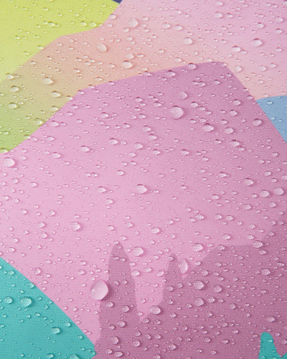 Macro detail of the grey, pink, and pastel mountain print Reimatec fabric used on the Reima Kiiruna girls' ski jacket, demonstrating its waterproof technology with dense water droplets beading and resting on the breathable surface.