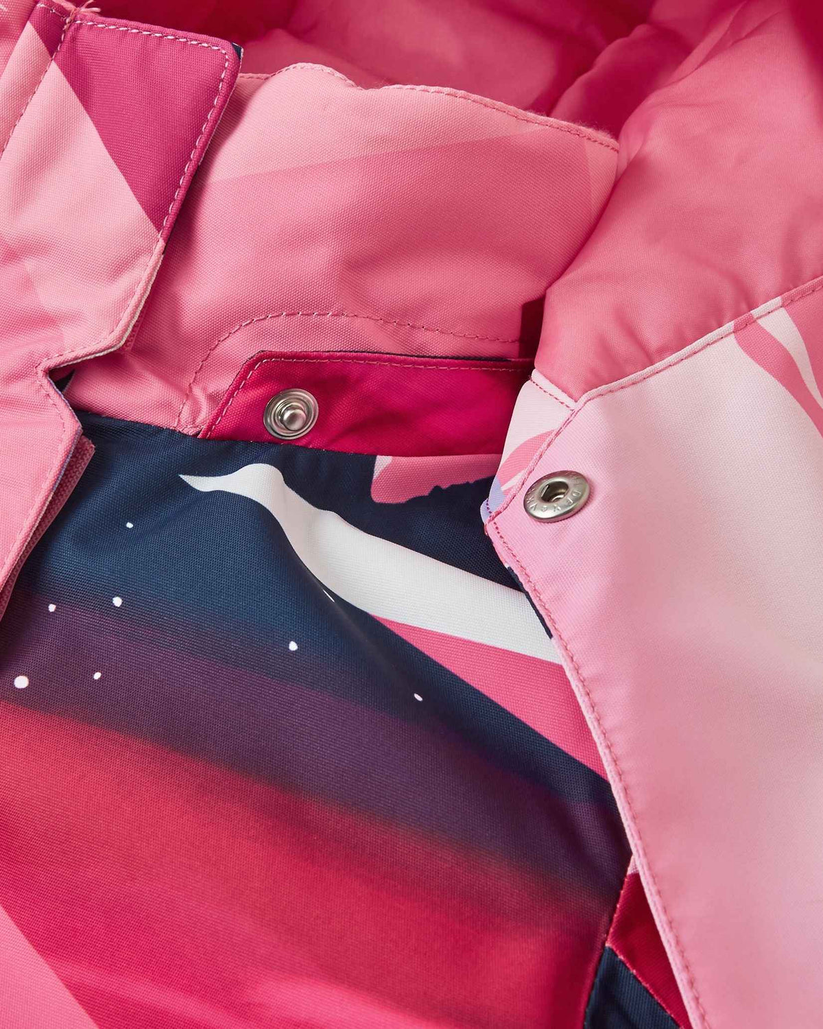 Detailed close-up of the tear-away metallic safety snaps connecting the hood to the collar of the soft coral Reima Kiiruna kids' winter coat, allowing for quick release if snagged during active outdoor play.