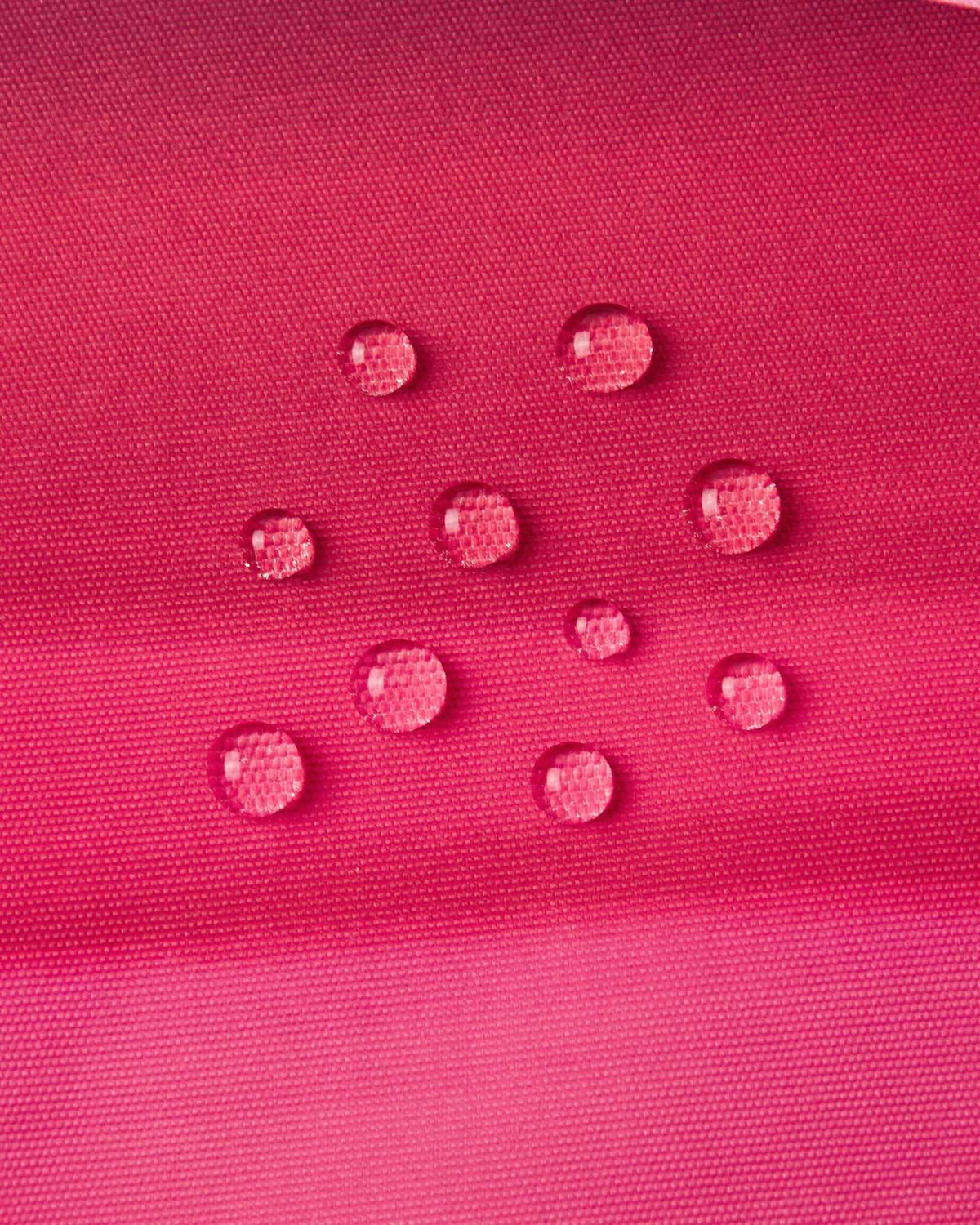 Macro close-up of water droplets forming tight beads on the soft coral pink outer fabric of the Reima Kiiruna ski jacket, demonstrating its fluorocarbon-free BIONIC-FINISH ECO dirt- and water-repellent coating.