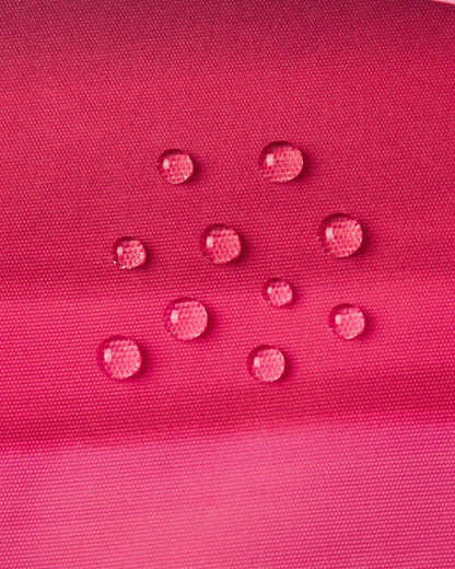 Macro close-up of water droplets forming tight beads on the soft coral pink outer fabric of the Reima Kiiruna ski jacket, demonstrating its fluorocarbon-free BIONIC-FINISH ECO dirt- and water-repellent coating.
