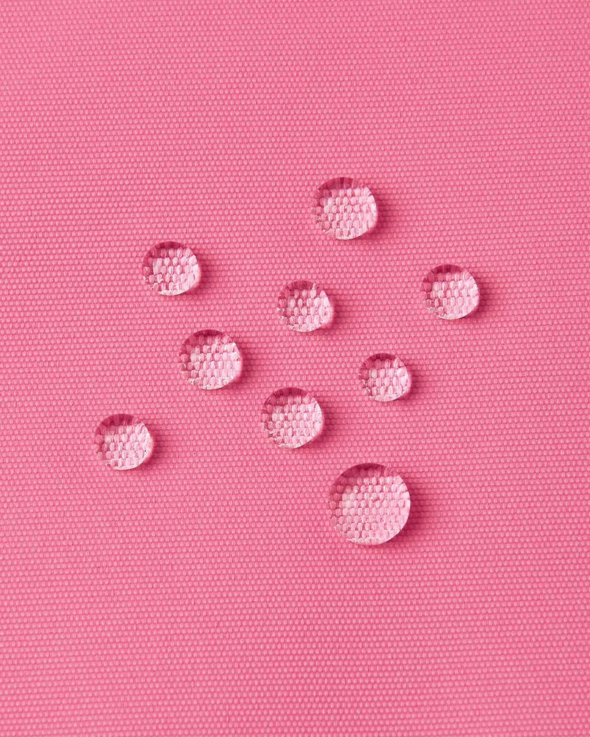 Macro close-up of water droplets forming tight beads on the solid soft coral outer fabric of the Reima Kiiruna ski jacket, emphasizing the fluorocarbon-free BIONIC-FINISH ECO water-repellent coating.