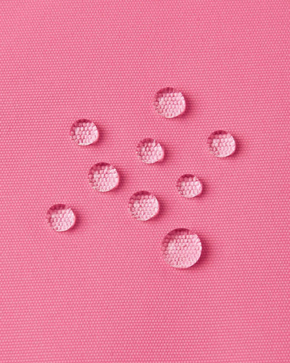 Macro close-up of water droplets forming tight beads on the solid soft coral outer fabric of the Reima Kiiruna ski jacket, emphasizing the fluorocarbon-free BIONIC-FINISH ECO water-repellent coating.