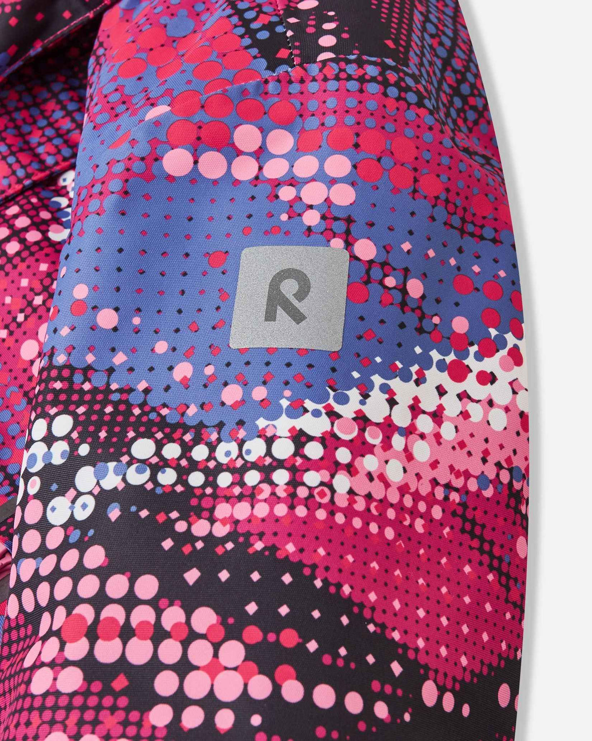 Close-up of the sleeve on the rosy berry patterned Reima Kiiruna youth ski jacket, featuring the reflective square Reima 'R' emblem for enhanced nighttime and low-light slope safety.