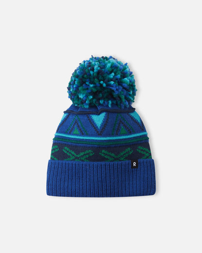 Alternate front flat lay view of the twilight blue Reima Kirjoen children's jacquard knit winter hat. The image showcases the premium merino wool-blend texture, the small woven black Reima logo tag on the hem, and the fun geometric winter design.