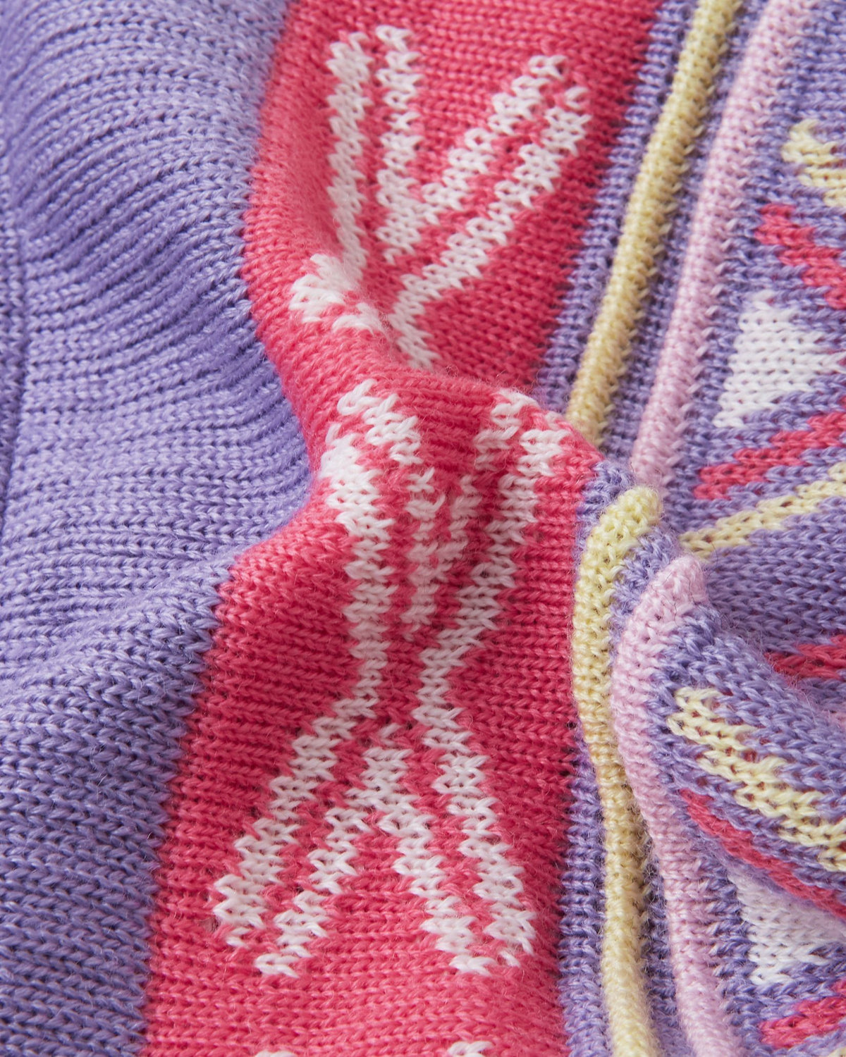 Macro close-up of the thick, colorful geometric jacquard knit structure on the blooming lilac Reima Kirjoen kids' winter hat, demonstrating the high-quality texture and flexibility of the warm merino wool-blend yarn.