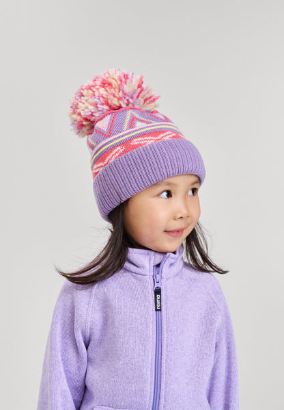 Lifestyle portrait of a young girl smiling while wearing the blooming lilac Reima Kirjoen kids' merino wool beanie paired with a matching fleece jacket. The image demonstrates how the ribbed hem provides a secure, warm fit for optimal thermal control.