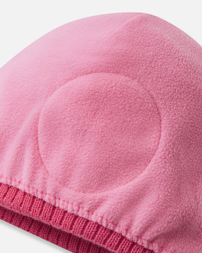 Detailed interior view of the soft coral Reima Kirjoen kids' winter beanie. The image reveals the fully lined, soft thermal fleece interior and the specialized circular windproof earpiece inserts engineered to protect children's ears from cold winter winds.