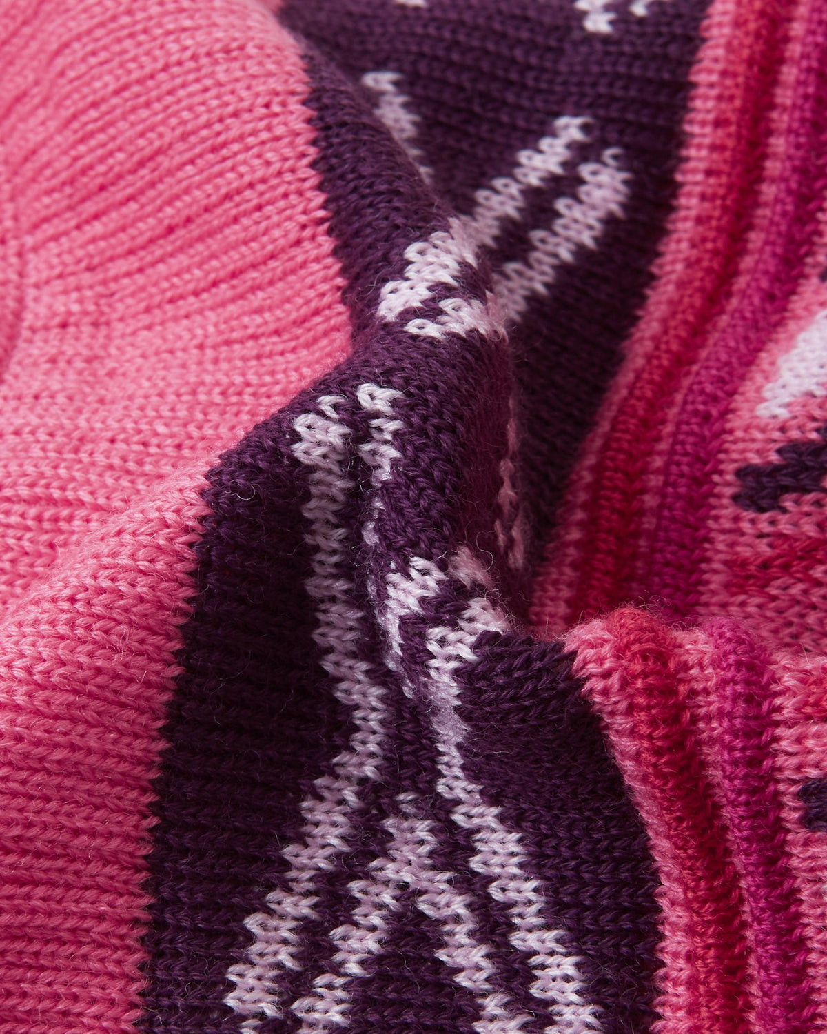 Macro close-up of the thick, colorful geometric jacquard knit structure on the soft coral pink Reima Kirjoen kids' winter hat, demonstrating the high-quality texture and flexibility of the warm merino wool-blend yarn.