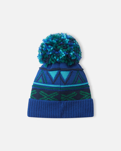 Back flat lay view of the twilight blue Reima Kirjoen kids' merino wool beanie, displaying the continuous seamless geometric jacquard knit pattern and the cozy, colorful yarn pom-pom designed to retain body heat in cold weather.