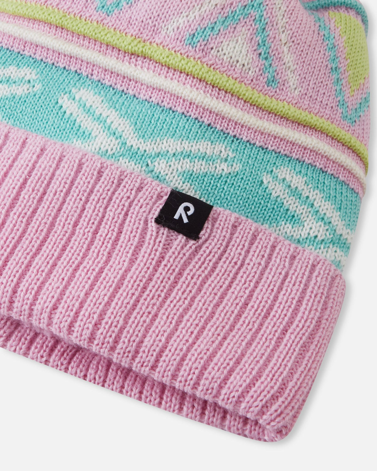 Close-up macro detail of the Reima Kirjoen kids' winter hat, showcasing the fine merino wool jacquard knit in teal and white, ribbed fold-over brim, and woven black Reima logo badge.