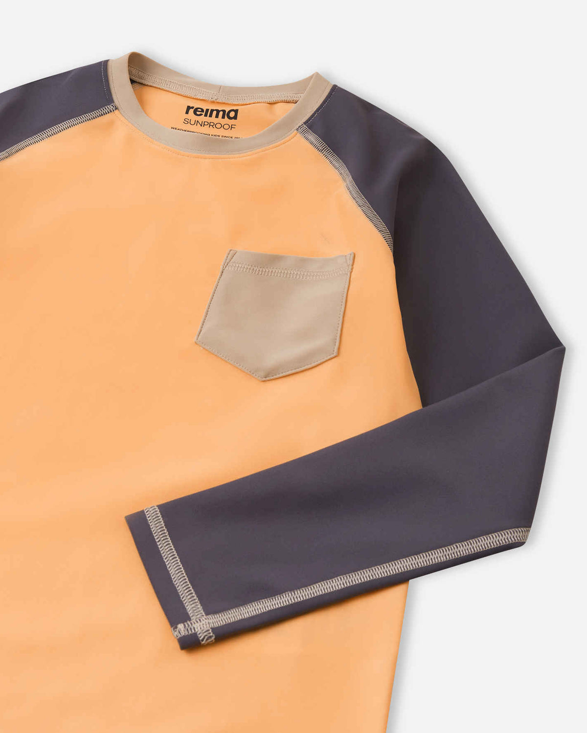 Detailed close-up of the Reima Kroolaus kids' apricot sunproof rash guard, focusing on the beige chest pocket, durable flatlock stitching, and the protective Reima Sunproof neckline.