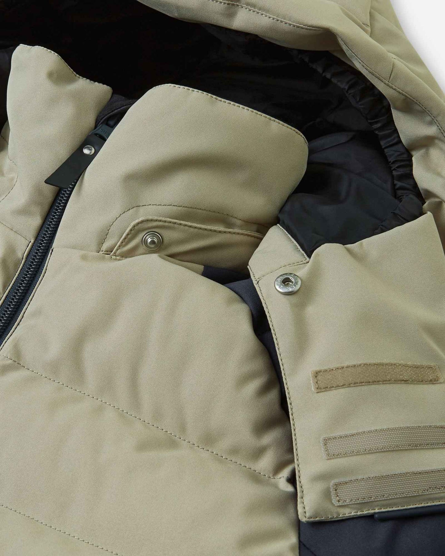 Close-up of the collar area on the Reima Kuosku kids ski jacket in Soft black, detailing the secure snap buttons used to attach the safe, removable hood.