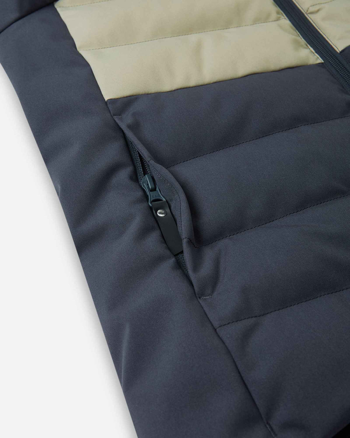 Close-up detail of the secure, hidden front zippered pocket on the quilted body of the Reima Kuosku kids ski jacket in Soft black.